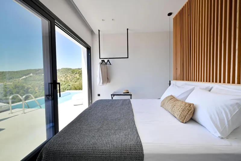 A double bed with an oak-slat wall, facing glass doors to the pool and the sea