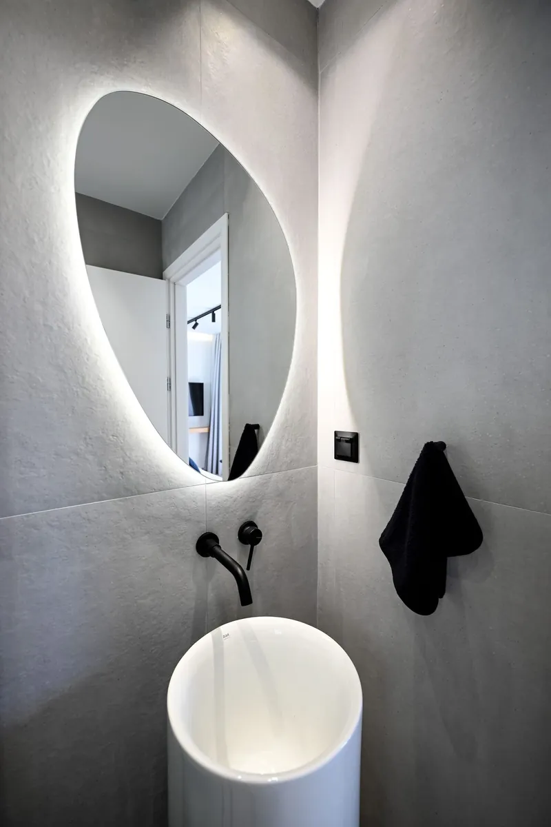 The round lit mirror above a white pedestal basin