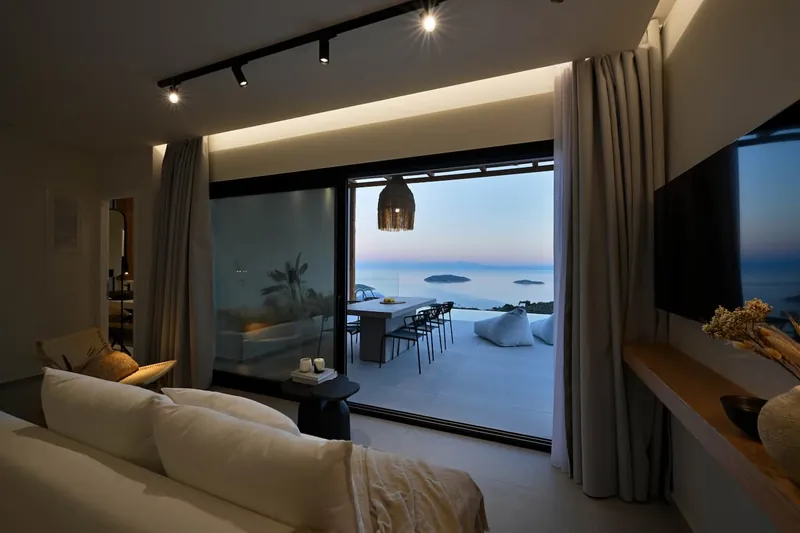 The living room opening onto the terrace and the sea at dusk