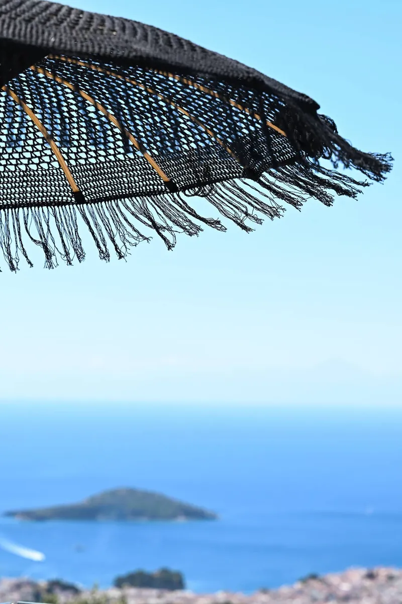 The fringe of the black parasol against the sky, an islet below