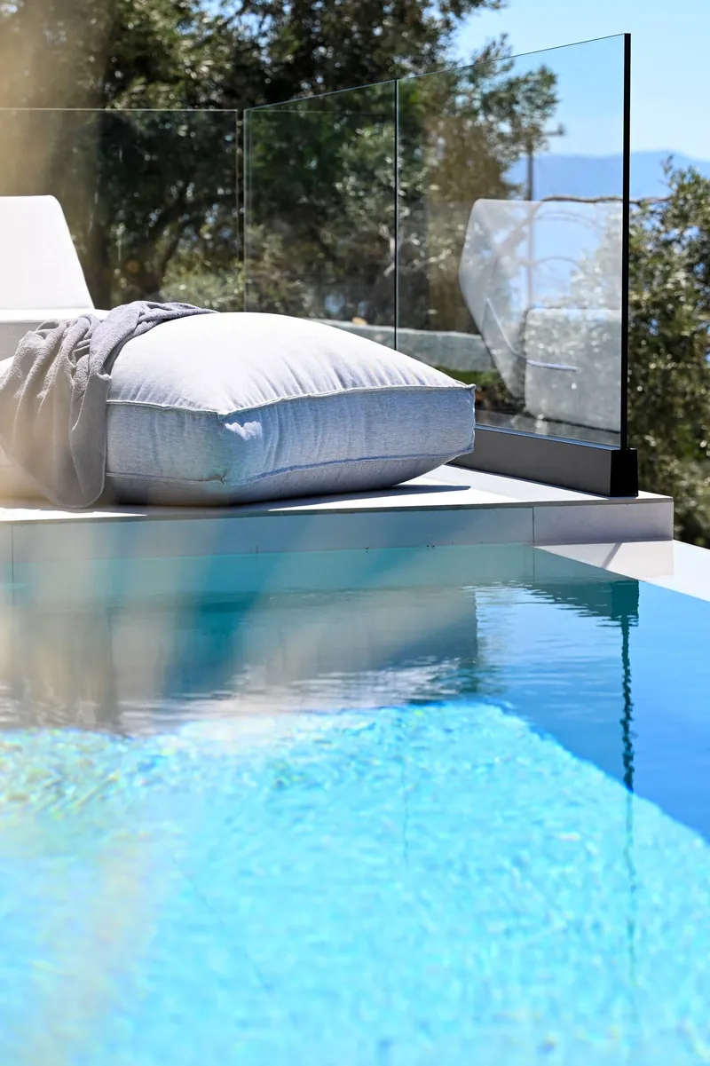 A day bed on the pool’s edge, behind the glass balustrade
