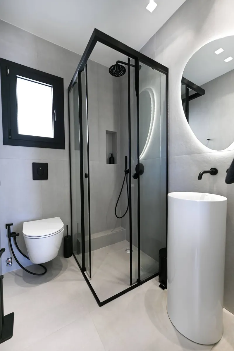 The second bathroom, with a glass shower and a round lit mirror