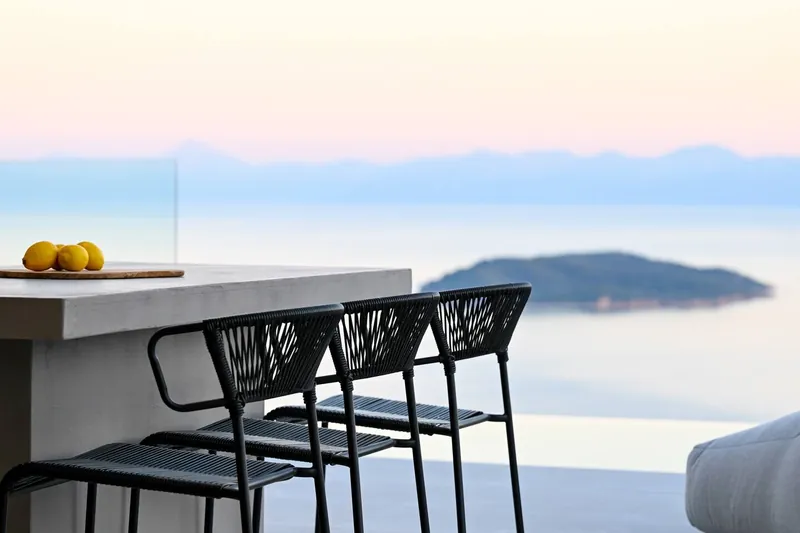 The terrace bar and its stools at dusk, an islet on a still pink sea